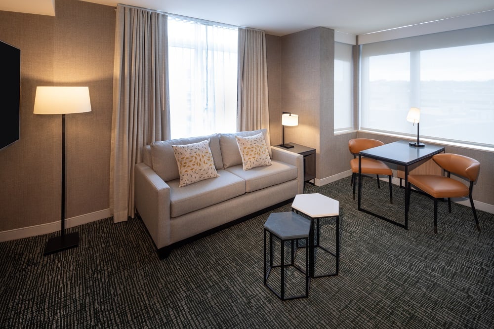 hotel room living area with couch and seating area and two large windows