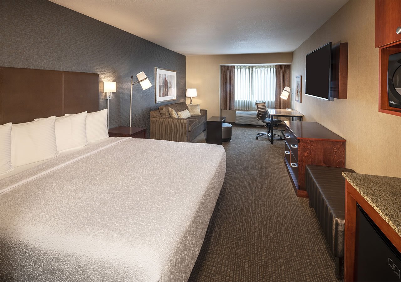 View of hotel room with large bed with white bedding, couch, desk and window