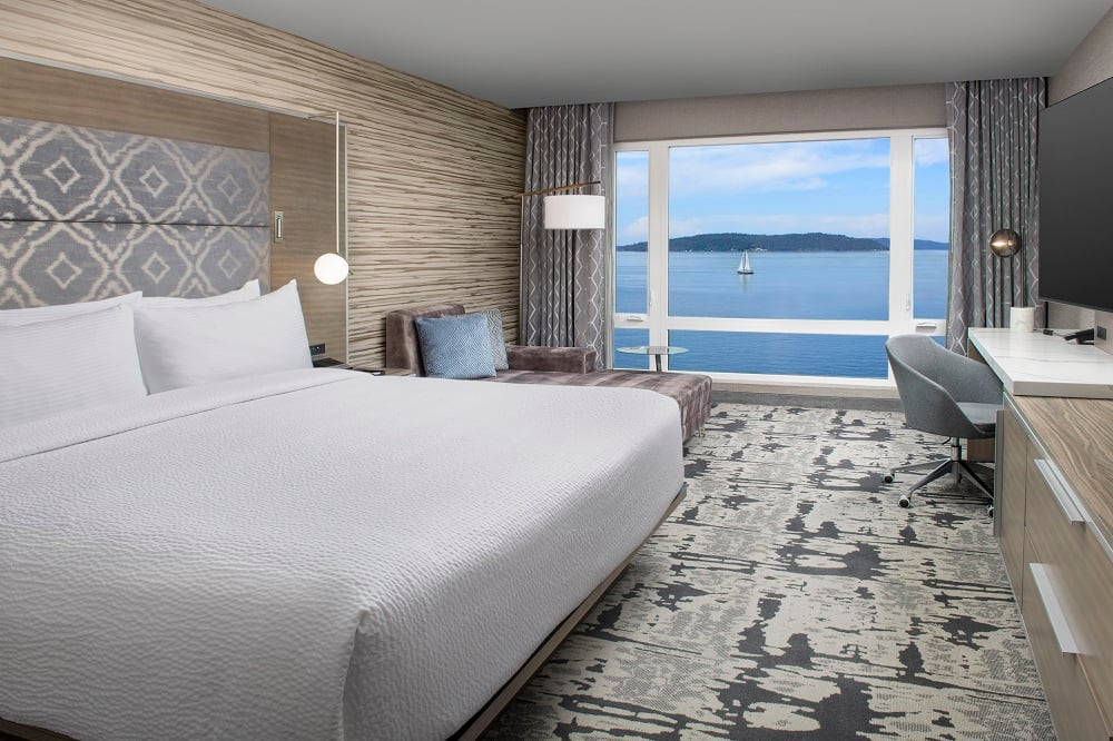 hotel room with king bed, lounge seating, desk and TV with large window facing water