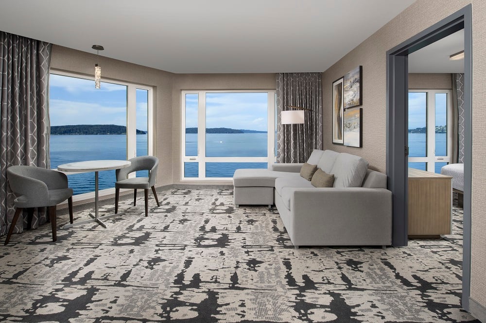 hotel room living space with couch, seating area and two large windows facing the water