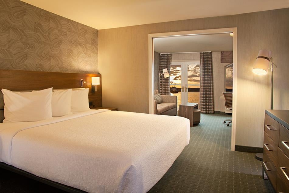 hotel room bedroom with king bed in foreground and living space through doorway in background