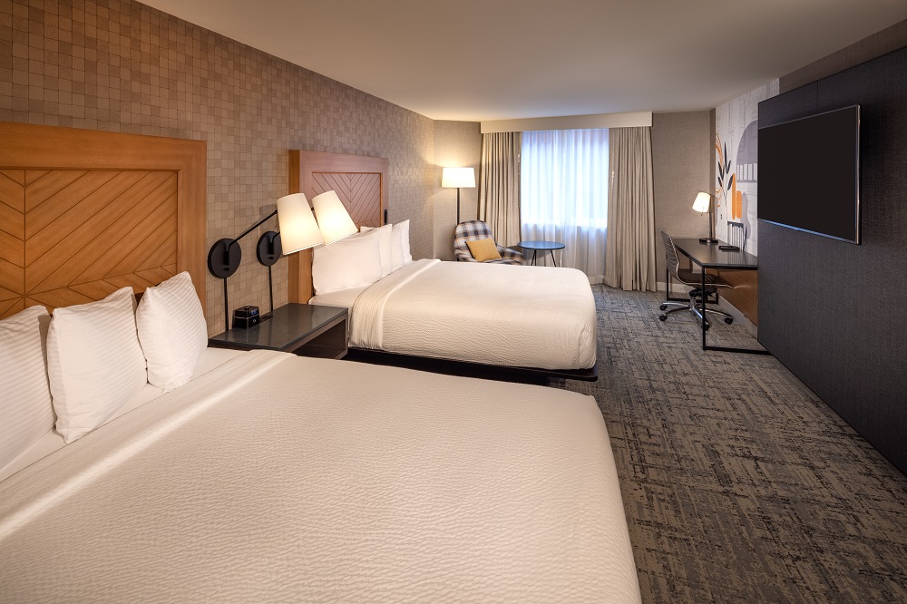 hotel room with two queen beds, desk, chair and window.