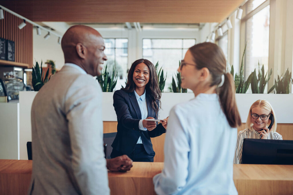Friendly young African American concierge working at a reception counter giving room information to two guests checking into a hotel.