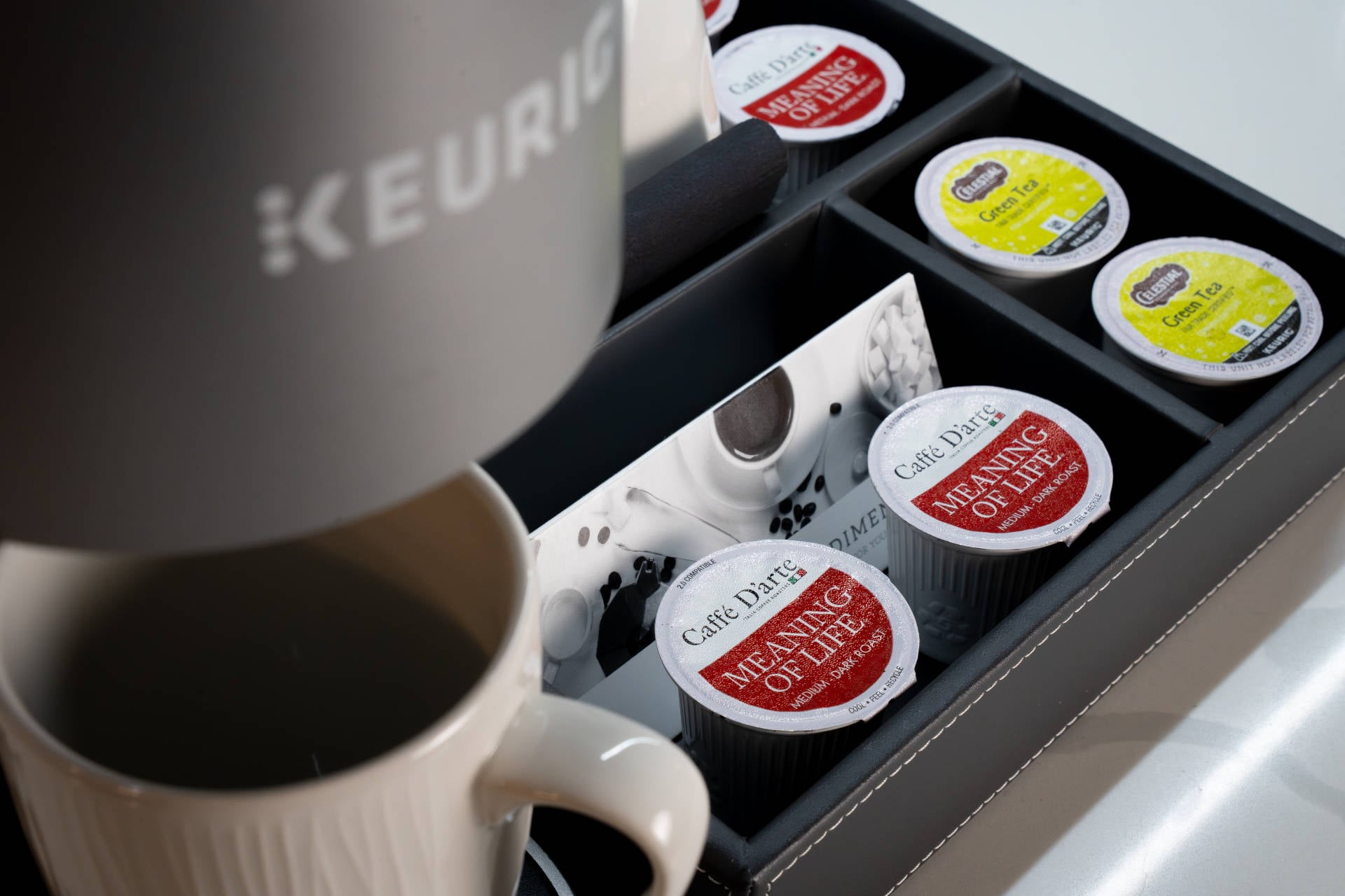 Keurig coffee maker brewing a cup beside an in-room hospitality tray with assorted coffee pods and condiments at Silver Cloud Hotel Portland.