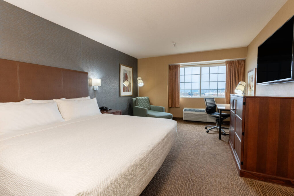 King bed guestroom at Silver Cloud Hotel Portland featuring a plush white bed, work desk, seating area, and large window with natural light.