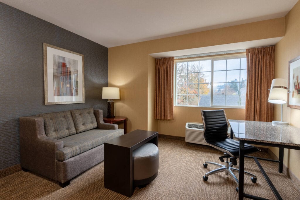 Mini Suite at Silver Cloud Hotel Portland featuring a separate sitting area with sofa, work desk, and large window bringing in natural light.
